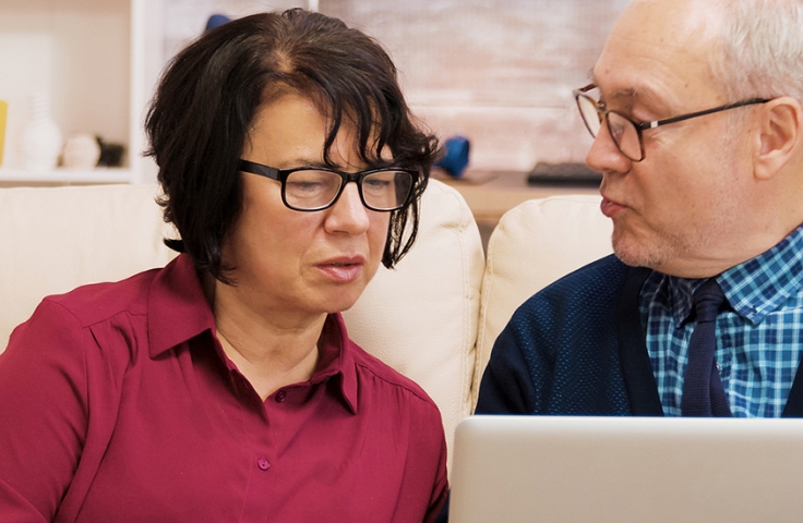 Older couple sitting on sofa looking at laptop