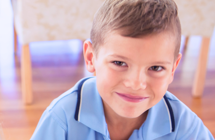Close crop of a school-aged child smiling at camera in a domestic setting.